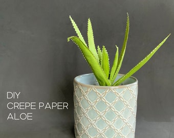 May include: A DIY crepe paper aloe plant with bright green, serrated leaves housed in a cylindrical ceramic pot featuring a light blue and white interlocking geometric lattice pattern. The text DIY CREPE PAPER ALOE is visible on the left.