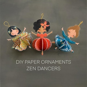 Op de afbeelding: Drie doe-het-zelf papieren ornamenten van dansende figuren. De figuren hebben lachende gezichten en dragen kleurrijke jurken. De tekst "DIY PAPER ORNAMENTS ZEN DANCERS" is eronder in het wit gedrukt.