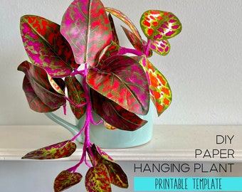 May include: A DIY paper hanging plant with vibrant pink, red, and green patterned leaves on bright pink stems, displayed in a light blue ceramic pot. The text DIY PAPER HANGING PLANT PRINTABLE TEMPLATE is visible in the lower right corner.