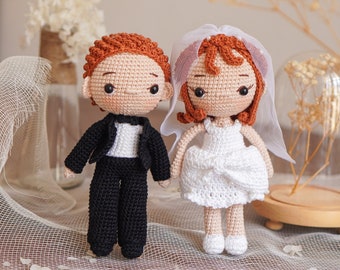 May include: A crocheted bride and groom doll set. The bride is wearing a white dress and a veil. The groom is wearing a black suit with a white shirt and a black bow tie.