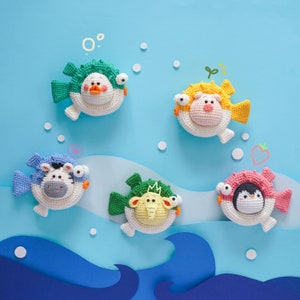May include: Five crocheted plush pufferfish toys in various colours and designs. The pufferfish are arranged on a blue background with white dots.