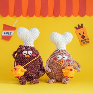 May include: Two crocheted plush toys shaped like chicken legs. The toys are brown and have white accents. One toy is holding a small yellow crocheted chick. The toys are on a yellow background with a red and white striped awning above them.