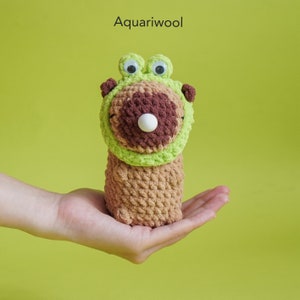 May include: A crocheted stuffed toy frog with brown and green yarn. The frog has large googly eyes and a white button nose.