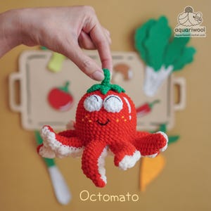 Puede incluir: Un juguete "Octomato" rojo tejido a mano, una combinación caprichosa de un pulpo y un tomate. El juguete tiene detalles blancos en sus tentáculos y un tallo verde. La imagen incluye un fondo con recortes de comida de fieltro y el texto "aquariwool.com".