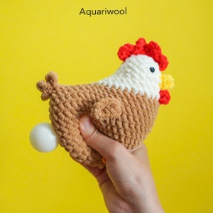 May include: A crocheted brown and white chicken toy with a red comb and yellow beak, holding a white egg. The toy is made with a soft, fuzzy yarn.