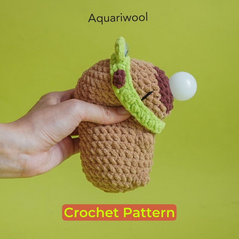 May include: Crochet pattern for a brown avocado plush toy with a green felt hat and a white felt seed. The pattern is called "Aquariwool Crochet Pattern".