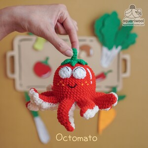 May include: A handmade red crocheted "Octomato" toy, a whimsical combination of an octopus and a tomato, with white accents and a green stem. The toy has smiling eyes and is held up against a backdrop of felt food cutouts.