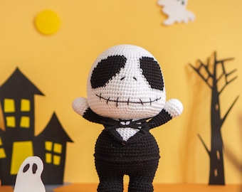 May include: A crocheted Jack Skellington doll wearing a black suit and a white bow tie. The doll is standing on a table with a yellow background.