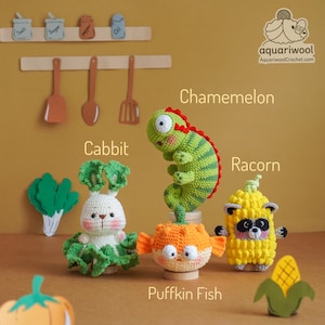 May include: A collection of handmade crochet amigurumi toys, including a green and red chameleon, a white rabbit with green lettuce, an orange pufferfish, and a yellow raccoon. The toys are displayed on a yellow background.