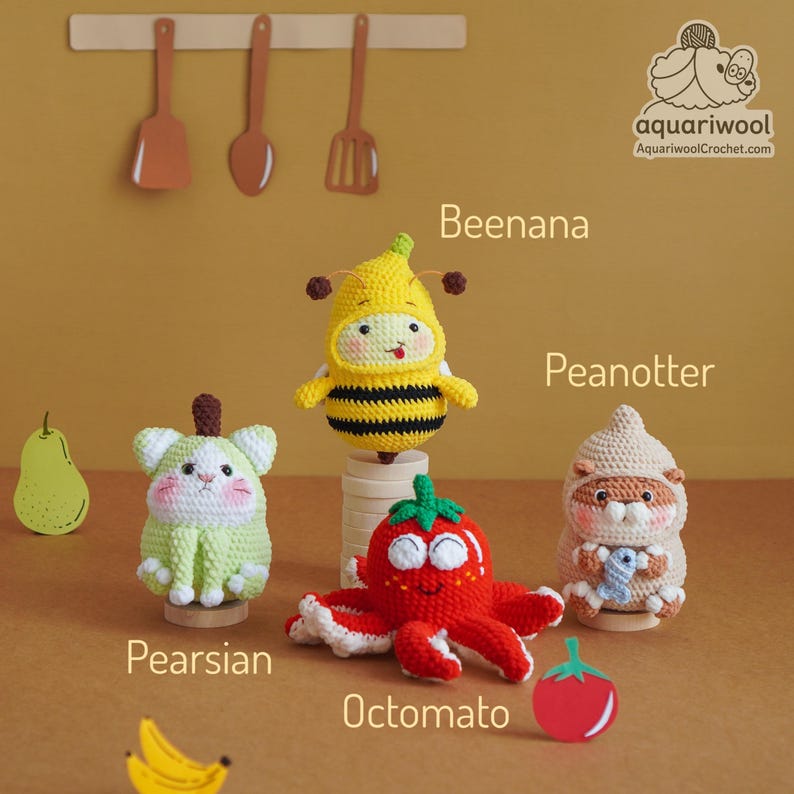 May include: A collection of handmade crochet amigurumi toys, including a bee-banana hybrid, a strawberry octopus, a pear-shaped cat, and a hamster-like creature. The toys are displayed on a light brown surface.
