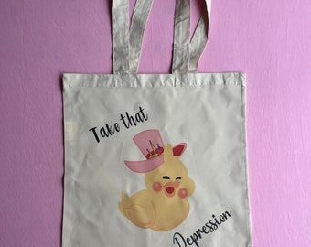 May include: A white tote bag with a yellow cartoon duck wearing a pink hat with a crown. The text "Take that Depression" is printed on the bag.