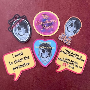 May include: A selection of vibrant stickers with diverse designs and text. One sticker displays a stylized ear with the words "Urraghh EMOTIONS!!". Other stickers include phrases such as "Sanctuary Moon" and "You're my favourite human".