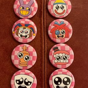 Könnte beinhalten: Acht runde Buttons mit Cartoon-Charakter-Designs auf einem rosa-weiß karierten Hintergrund. Die Charaktere haben verschiedene Ausdrücke und Stile, darunter ein Hase, ein Clown und ein Narr. Die Buttons sind in zwei Reihen angeordnet.