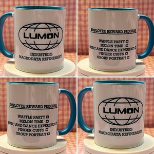 May include: White ceramic mug with a teal handle and rim. The mug features the text "LUMON" in a black oval design, with "INDUSTRIES MACRODATA REFINEMENT" below. Another mug shows "EMPLOYEE REWARD PROGRAM" and a list of activities.