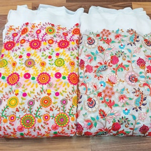 May include: Two white fabric pieces with colorful floral embroidery. One features yellow, orange, and pink flowers, while the other showcases red, pink, and blue floral patterns. The embroidery is detailed and vibrant.