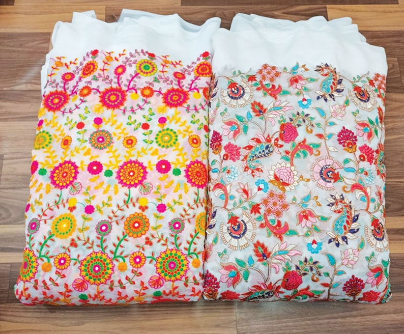May include: Two white fabric pieces with colorful floral embroidery. One features yellow, orange, and pink flowers, while the other showcases red, pink, and blue floral patterns. The embroidery is detailed and vibrant.