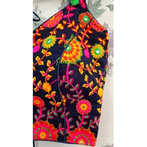 May include: A navy blue halter top with vibrant floral embroidery. The embroidery features pink, yellow, orange, and green flowers and leaves. The top has a simple design with a halter neck and a straight hemline.