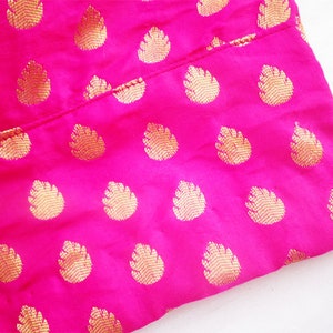 May include: Close-up of a vibrant pink fabric with a repeating gold leaf pattern. The fabric is folded, revealing the texture and sheen of the material. The gold pattern adds a touch of elegance to the bright pink background.
