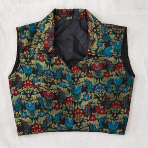 May include: A sleeveless vest featuring a black background with a floral pattern in red, blue, and gold. The vest has a collared neckline and a V-neck design. The fabric appears to be a woven brocade.