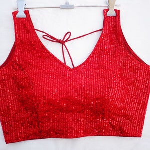 Puede incluir: Una blusa roja sin mangas con lentejuelas, cuello en V y lazada en la espalda.