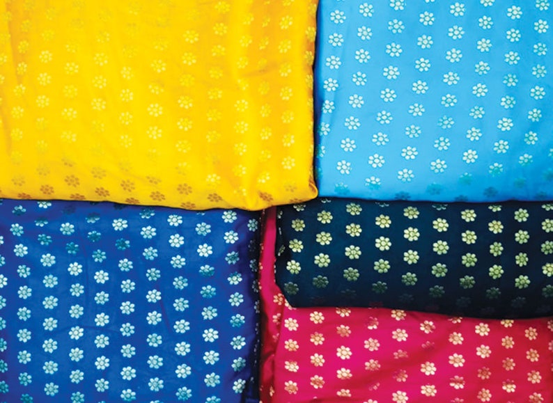 May include: A collection of colorful fabrics, each with a repeating floral pattern. The colors include yellow, light blue, dark blue, dark green, and pink. The fabric appears to be silk or a similar material.