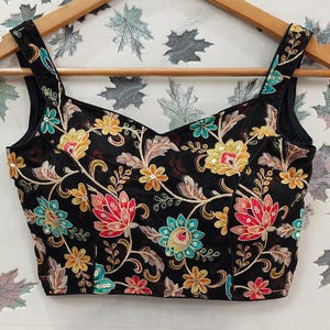 May include: A black embroidered crop top with a sweetheart neckline and floral pattern. The embroidery features colourful flowers and leaves on a black sheer fabric.