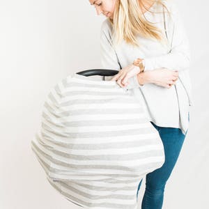 May include: A grey and white striped car seat cover with a woman holding it in front of a white background.