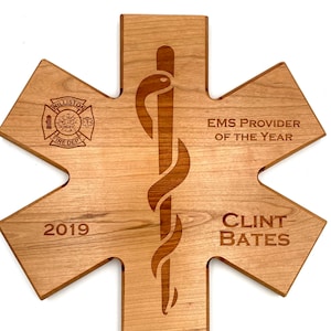 May include: A wooden star-shaped plaque with a medical symbol, the text "EMS Provider of the Year", the year "2019", and the name "Clint Bates".