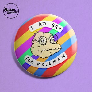 May include: A rainbow striped button with a cartoon character and the text "I am gay for Moleman".