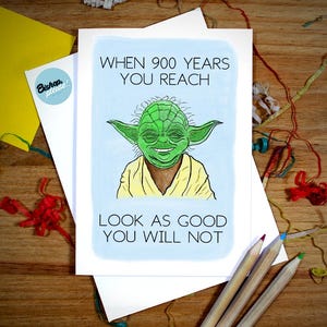 May include: Greeting card with a green Yoda illustration and the text "WHEN 900 YEARS YOU REACH LOOK AS GOOD YOU WILL NOT." The card is on a white envelope with a yellow paper and pencils.