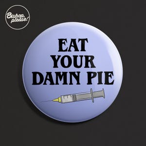 May include: A circular, pale blue badge with the words "EAT YOUR DAMN PIE" in black, bold text. A syringe graphic is below the text. The badge has a white circular logo in the upper left corner that says "Bishop, please!"