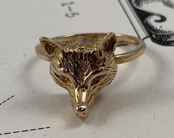 以下が含まれることがあります： 金色のリングに、精巧な狐の頭部のデザインが施されています。狐の頭部は正面を向いており、口は閉じられています。リングは金属製で、滑らかで磨かれた仕上げになっています。