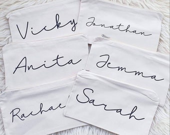 May include: Five white canvas zippered pouches with black cursive writing. The names on the pouches are Vicky, Jonathan, Anita, Jemma, and Sarah.