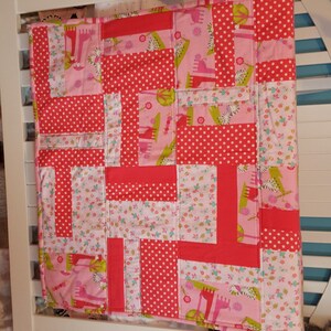 May include: A pink and red patchwork baby quilt with a giraffe print. The quilt is made of different fabrics with polka dots, flowers, and giraffes.
