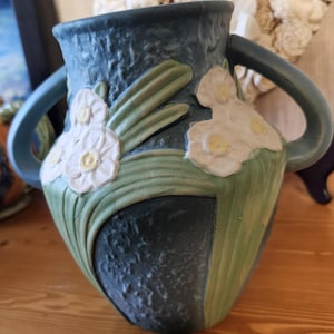 May include: A blue ceramic vase with two handles and white floral designs. The vase has a textured surface and is decorated with green leaves.