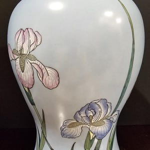 May include: A light blue ceramic vase with a bulbous body and a narrow neck. The vase is decorated with two iris flower designs in pink, purple, and green. The vase is approximately 12 inches tall.
