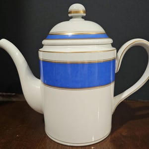 May include: White porcelain teapot with a blue and gold band around the body. The lid has a gold band around the top.
