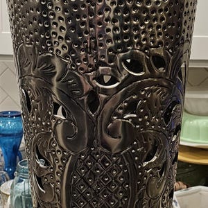 May include: A silver metal vase with an intricate floral design. The vase has a wide mouth and a narrow base. The design is embossed and cut out, creating a delicate and airy look.