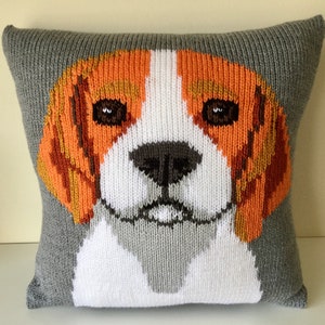 Könnte beinhalten: Ein graues gestricktes Kissen mit einem Beagle-Hundekopf, der auf die Vorderseite gestickt ist. Das Gesicht des Hundes ist weiß mit braunen und orangefarbenen Markierungen. Das Kissen ist eine großartige Ergänzung für jede Inneneinrichtung.