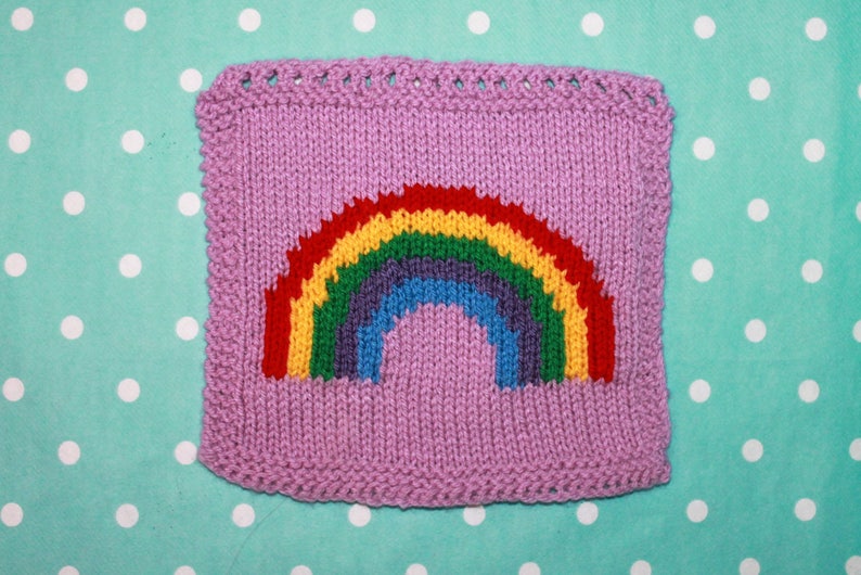 Puede incluir: Un cuadrado tejido con un dise&ntilde;o de arco&iacute;ris en rojo, naranja, amarillo, verde, azul, a&ntilde;il y violeta. El cuadrado es de color morado claro.
