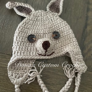 May include: A crocheted bunny hat with brown button eyes and a brown nose. The hat has a long crocheted tie that can be tied under the chin.
