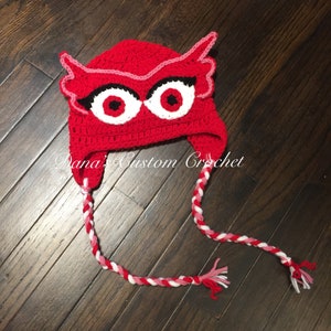 May include: Red crocheted owl hat with white and pink yarn braids. The hat features black eyes and a pink beak.