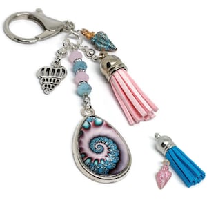 May include: A silver key chain with a pink and blue tassel, a blue and pink seashell charm, and a silver charm with a seashell design. The key chain also has a blue and pink spiral charm.