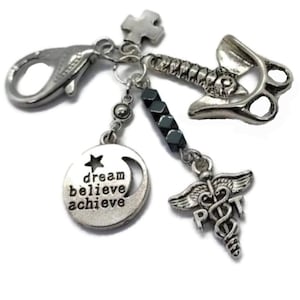 Puede incluir: Una pulsera de abalorios plateada con m&uacute;ltiples abalorios. Los abalorios incluyen una luna creciente con las palabras "dream believe achieve", un s&iacute;mbolo m&eacute;dico, un martillo y una cruz. La pulsera tiene un cierre de langosta.