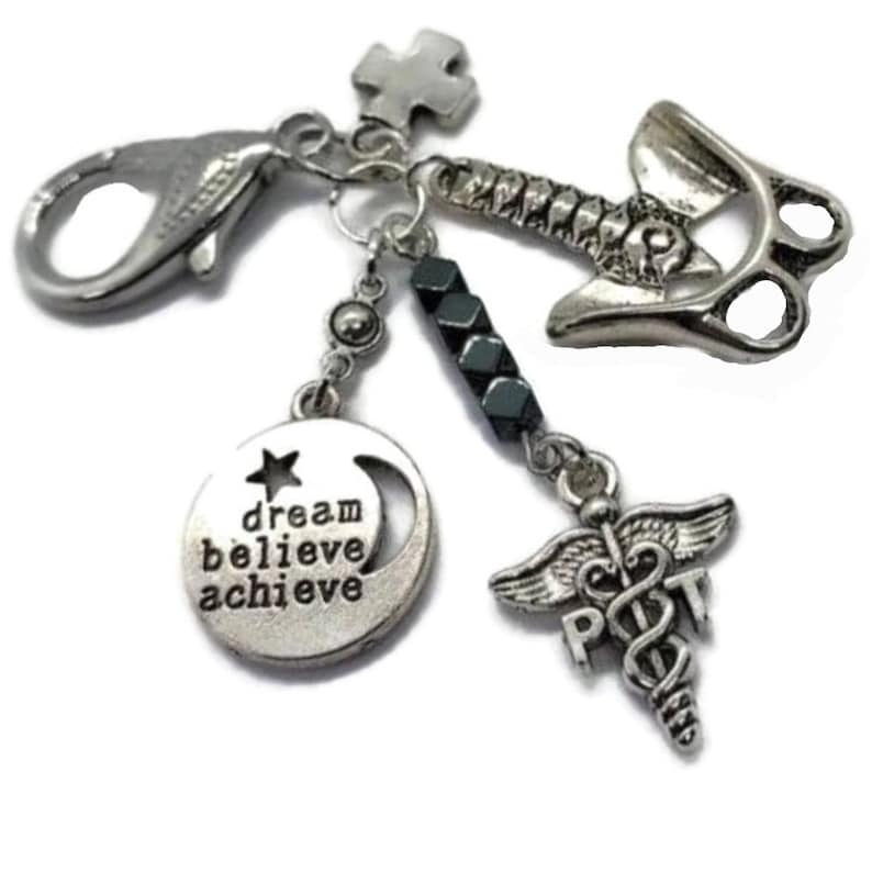 Puede incluir: Una pulsera de abalorios plateada con m&uacute;ltiples abalorios. Los abalorios incluyen una luna creciente con las palabras "dream believe achieve", un s&iacute;mbolo m&eacute;dico, un martillo y una cruz. La pulsera tiene un cierre de langosta.