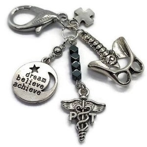 Puede incluir: Pulsera de dijes plateada con m&uacute;ltiples colgantes. Incluye un dije redondo con el texto "dream believe achieve", un s&iacute;mbolo m&eacute;dico, una columna vertebral y una pieza de rompecabezas. La pulsera tiene un cierre de langosta.