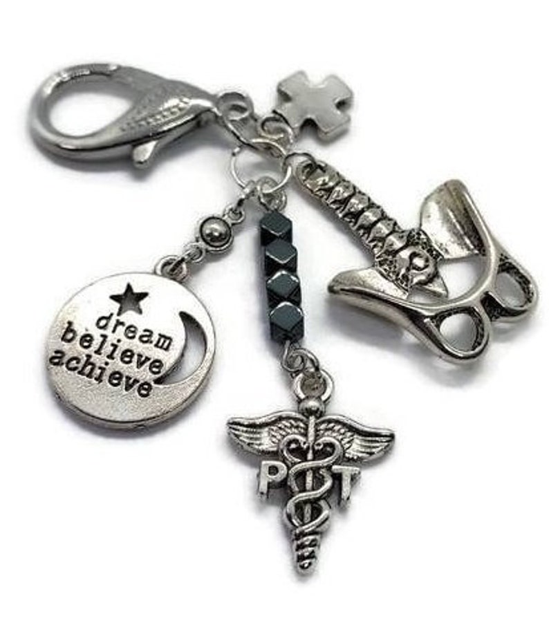 Puede incluir: Pulsera de dijes plateada con m&uacute;ltiples colgantes. Incluye un dije redondo con el texto "dream believe achieve", un s&iacute;mbolo m&eacute;dico, una columna vertebral y una pieza de rompecabezas. La pulsera tiene un cierre de langosta.