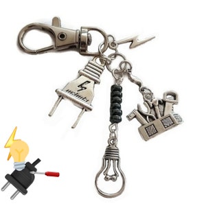 May include: Silver keychain featuring a lightbulb, a plug, a toolbox charm, and a black bead. The plug has a lightning bolt and the text "electrik" on it.
