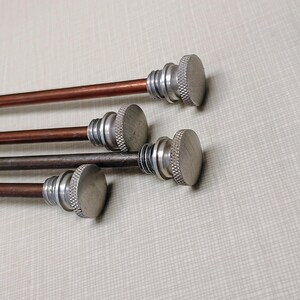 May include: Four curtain rods with metal finials. The rods are copper and dark brown, with silver-colored, circular finials at the ends. The rods are arranged diagonally against a light gray background.
