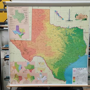 May include: A large, colorful map of Texas, mounted on a wooden roller. The map displays topographical features with a gradient of colors, and includes smaller inset maps and illustrations of landmarks. The word "TEXAS" is visible.